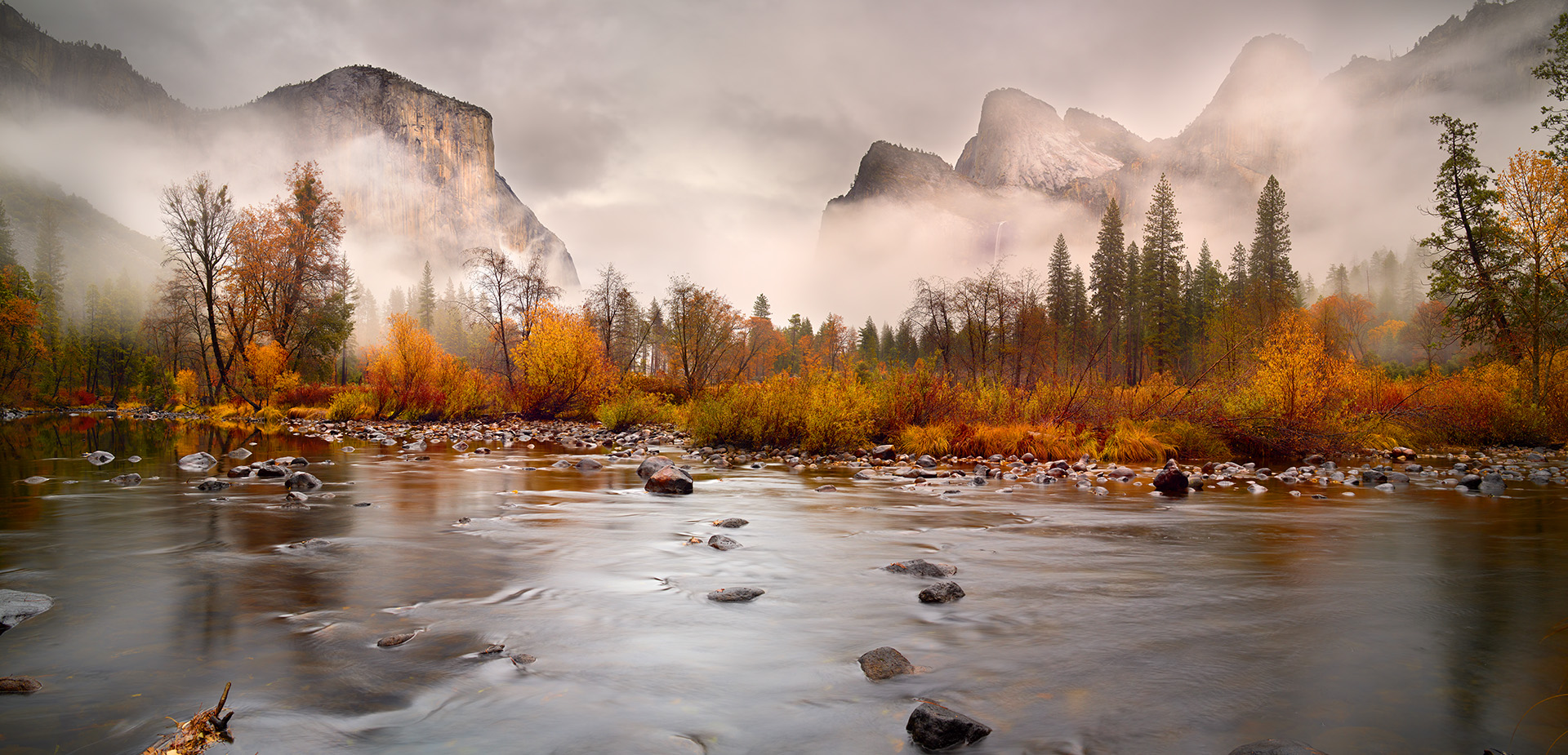 Yosemite National Park, a timeless treasure of dramatic cliffs, serene rivers, and vibrant autumn foliage, provided the perfect canvas for this image. Taken along the Merced River, this photograph showcases the park’s raw beauty at the end of fall, as the season transitions into winter. The golden hues of aspen and cottonwood trees, holding on to their last vibrant leaves, are juxtaposed against the looming granite monoliths veiled in mist, creating a dreamlike atmosphere.